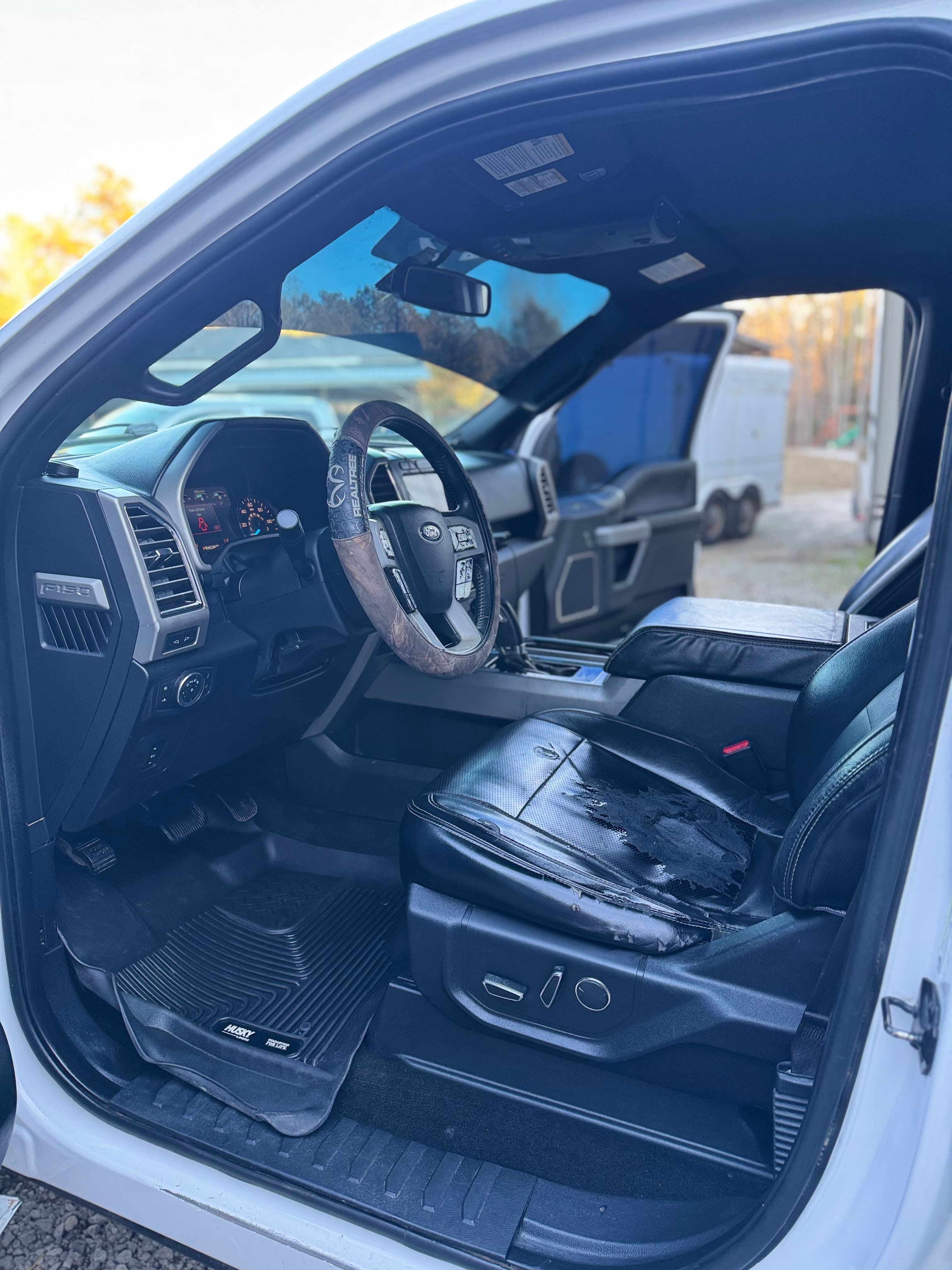Ford F-150 interior with a worn black leather seat and camouflage steering wheel cover.