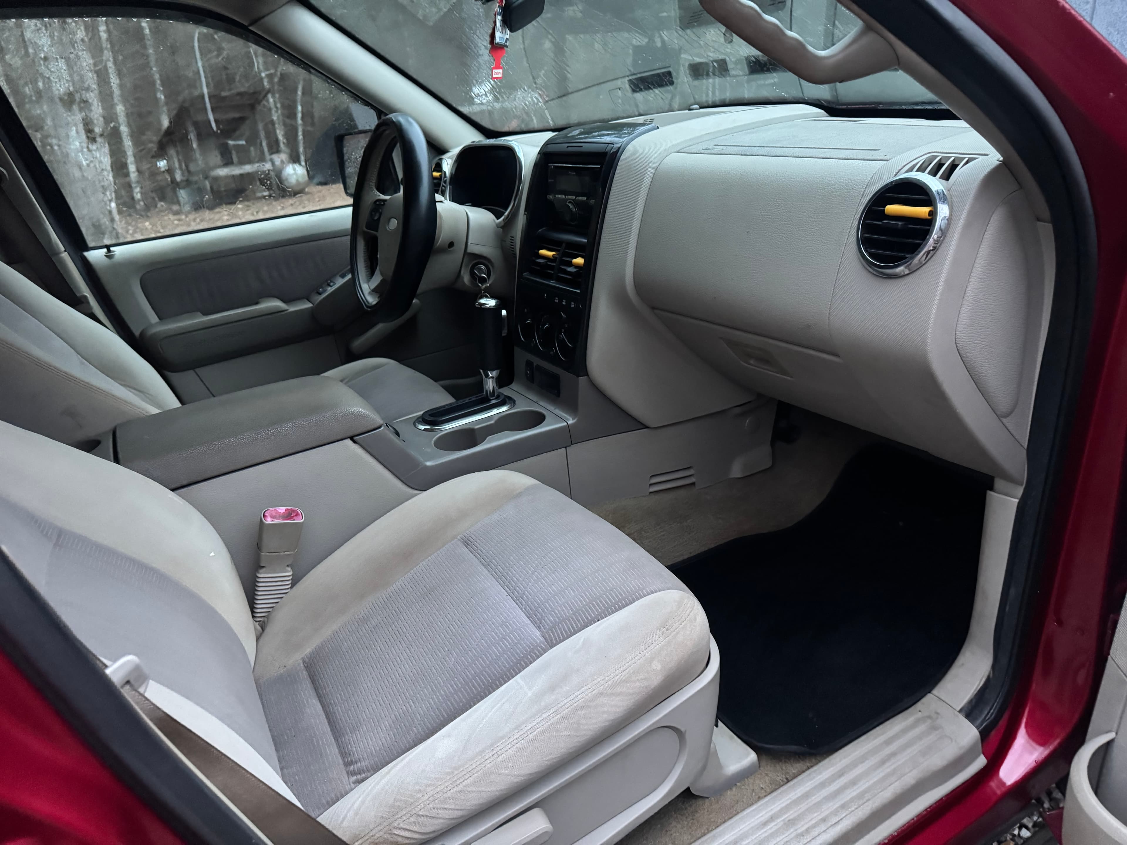 Interior of a red car with tan cloth seats, center console, and black steering wheel.