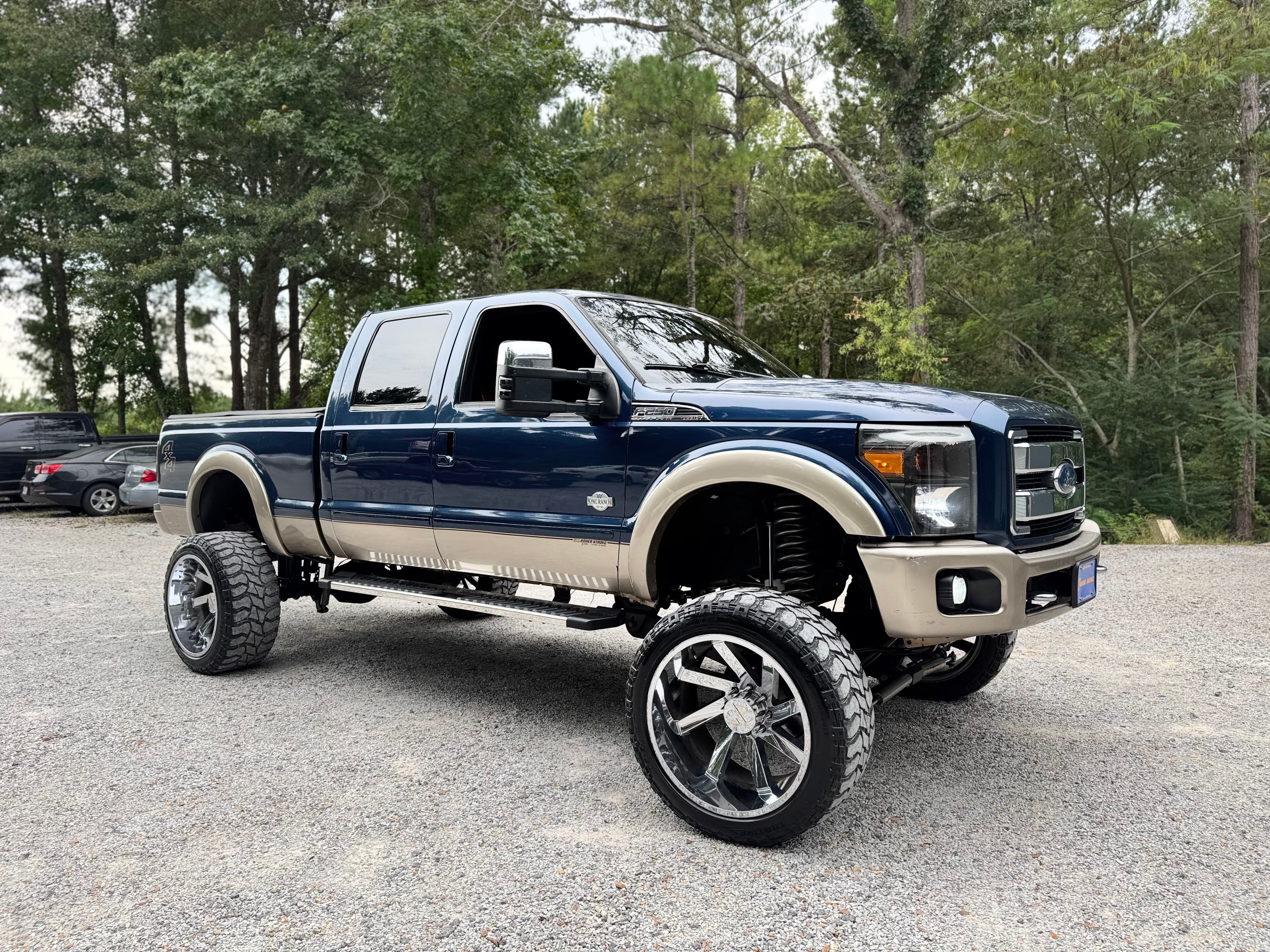 Lifted dark blue and tan Ford F-250 Super Duty truck with large chrome wheels.