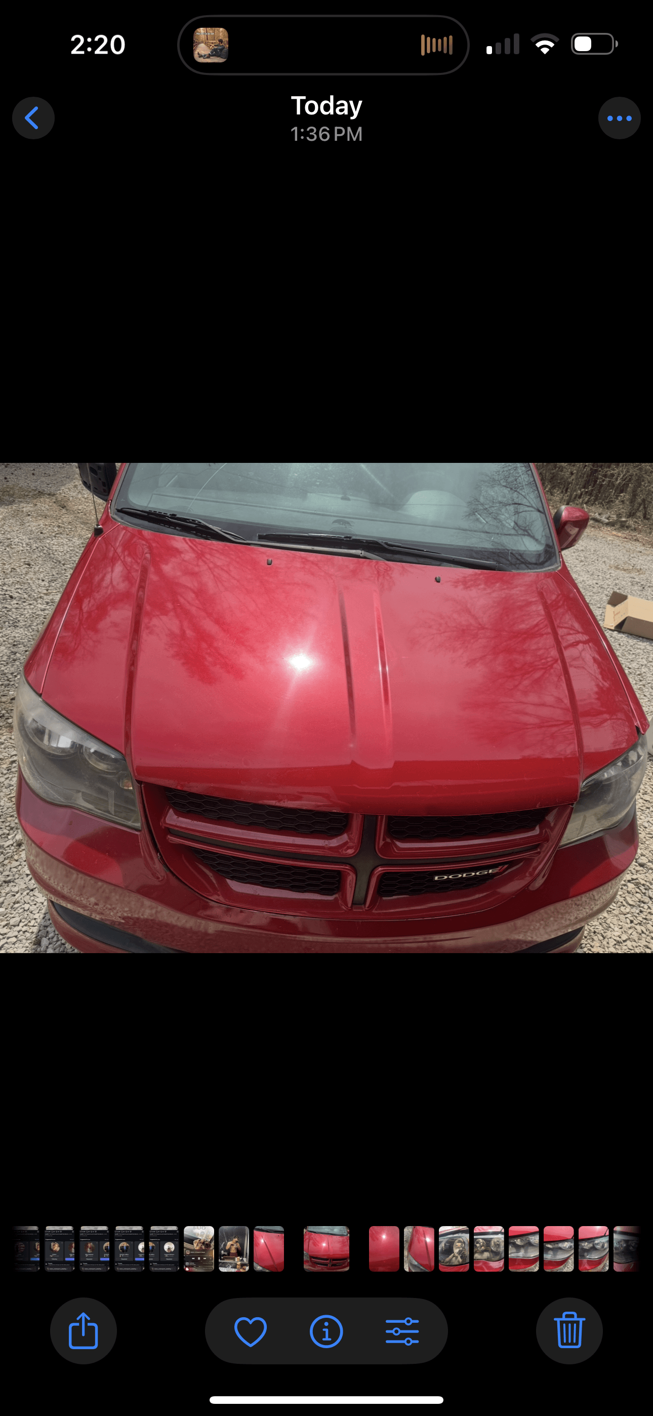 Close-up of a shiny red Dodge vehicle's hood and grille with a bright sun reflection.
