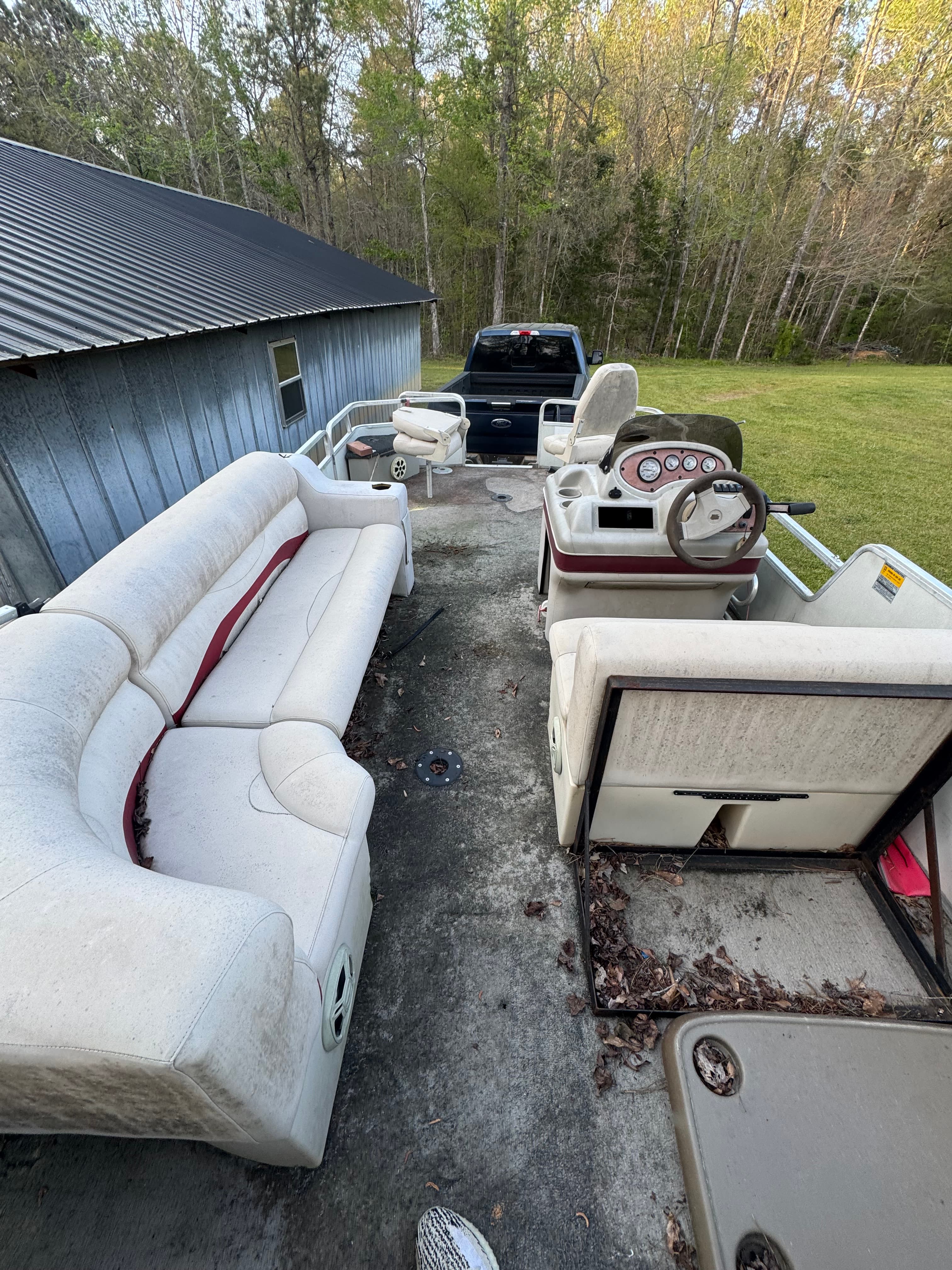 A dirty pontoon boat interior with stained white vinyl seating and a steering console.
