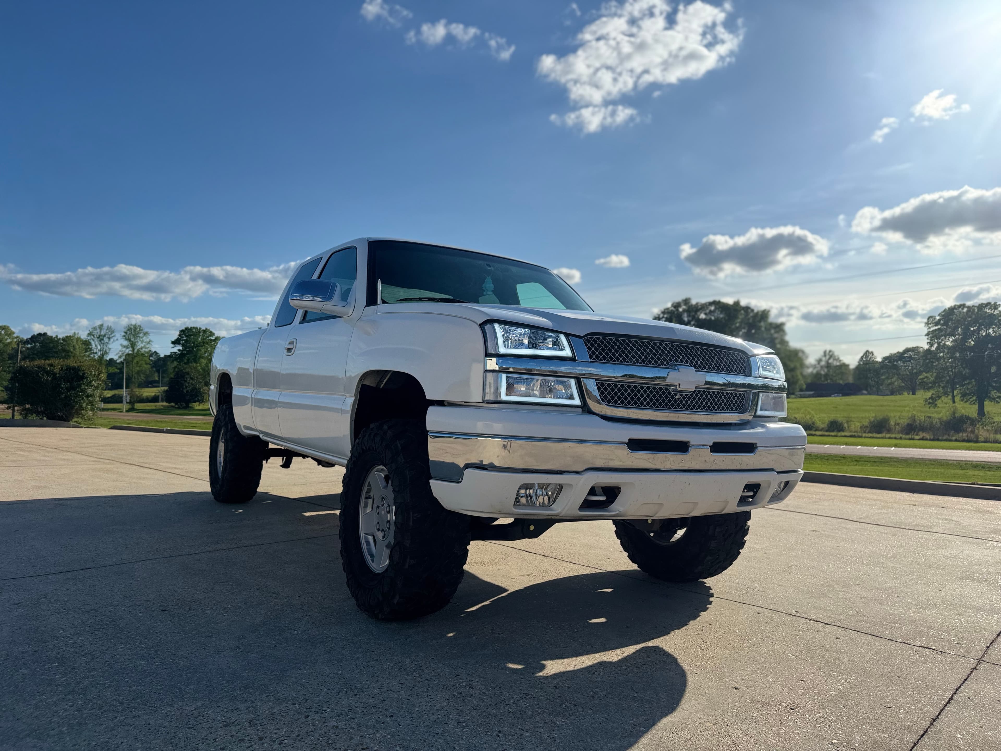 White lifted Chevrolet Silverado with large off-road tires parked on a sunny concrete lot.
