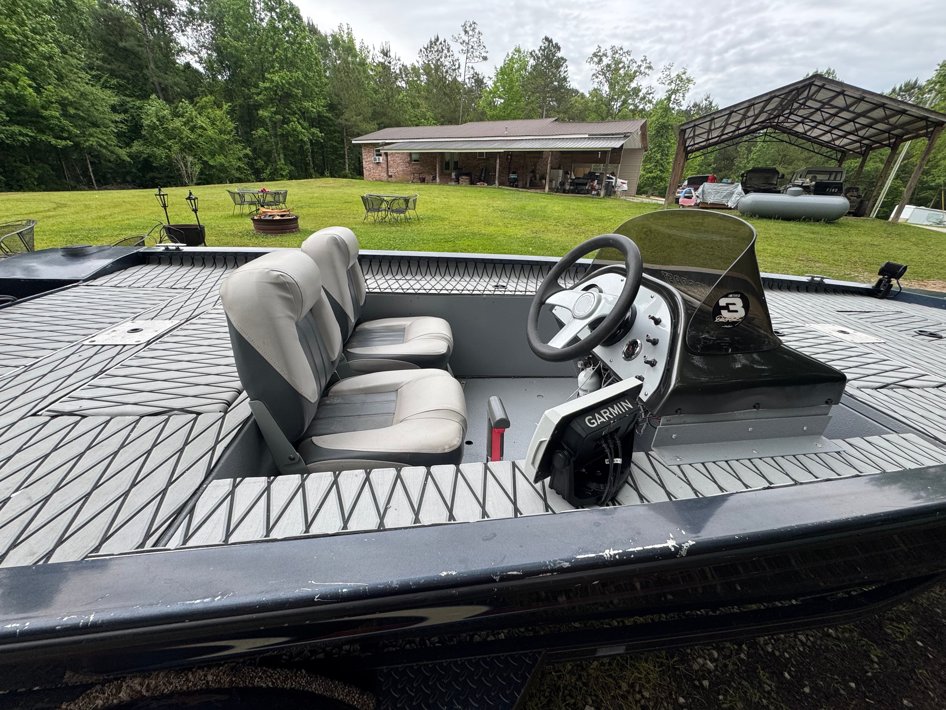 Interior of a motorboat with grey seats, steering wheel, and Garmin electronics on textured decking.
