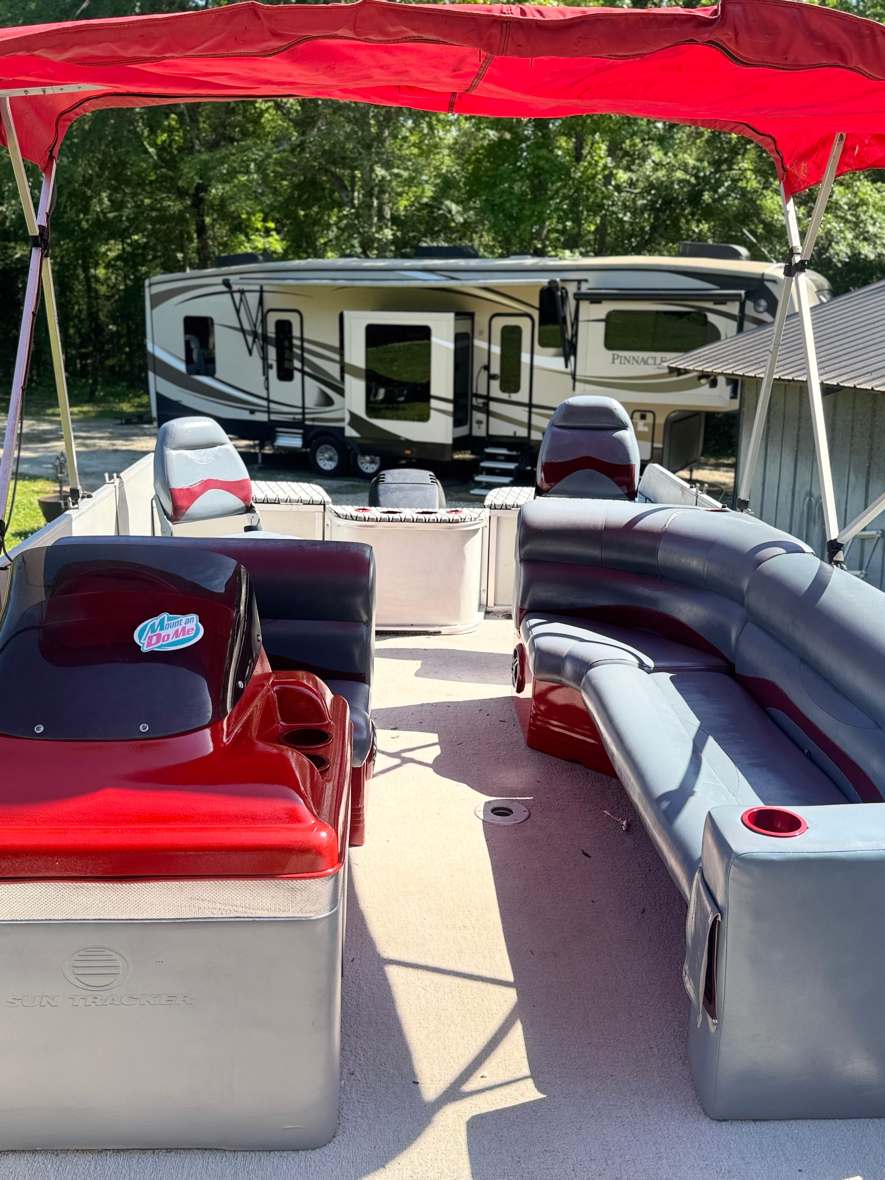 Red and grey Sun Tracker pontoon boat interior with a large RV in the background.