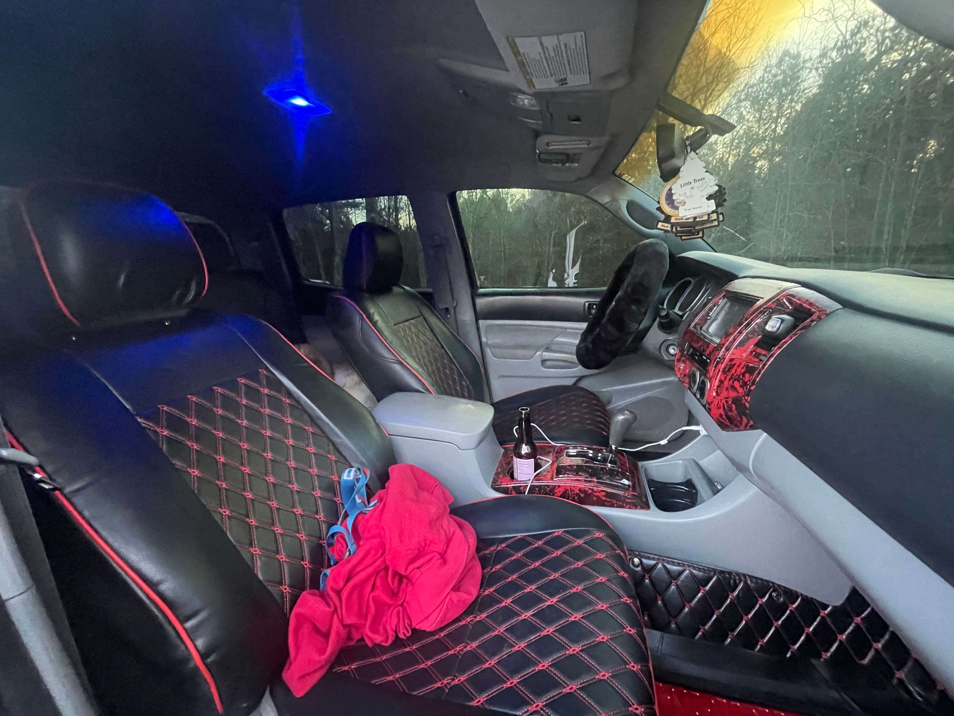 Custom vehicle interior featuring red diamond-stitched leather seats, red splatter trim, and blue ambient lighting.
